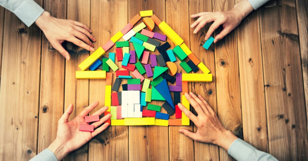 Many hands building a house out of building blocks